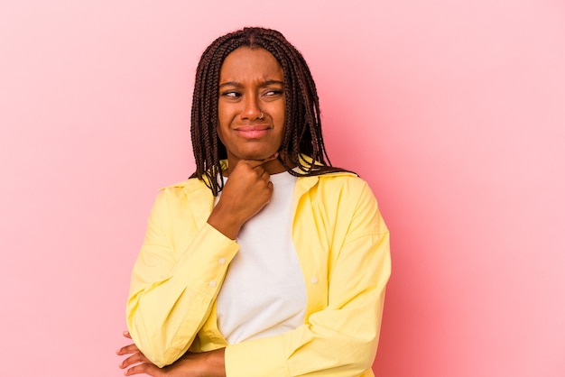 Joven afroamericana aislada sobre fondo rosa sufre dolor de garganta debido a un virus o infección.