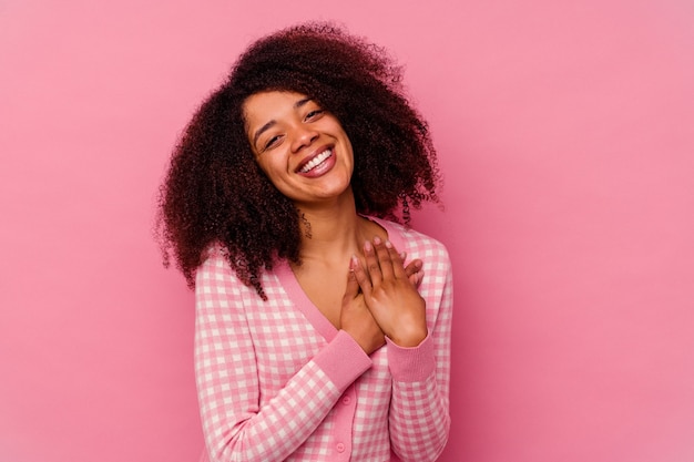 Joven afroamericana aislada sobre fondo rosa tiene una expresión amistosa, presionando la palma contra el pecho. Concepto de amor.