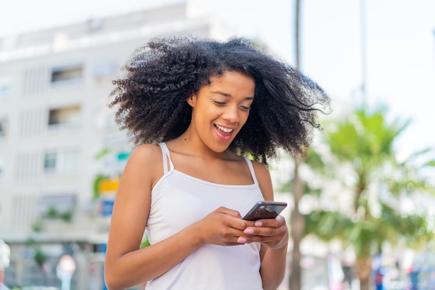 Una joven afroamericana al aire libre enviando un mensaje con el móvil