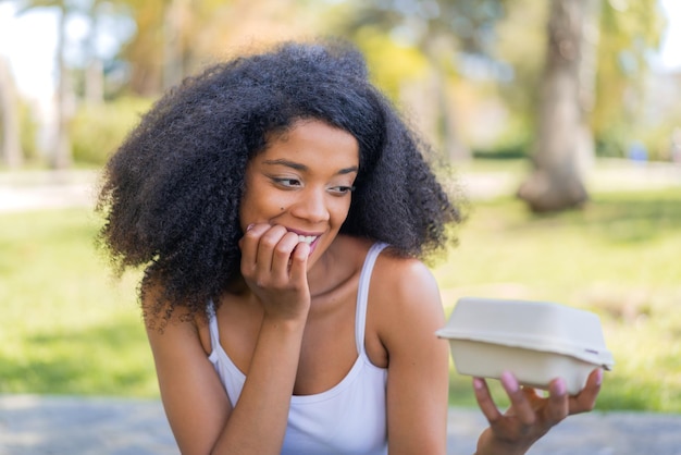 Una joven afroamericana al aire libre tomando una caja de comida para llevar