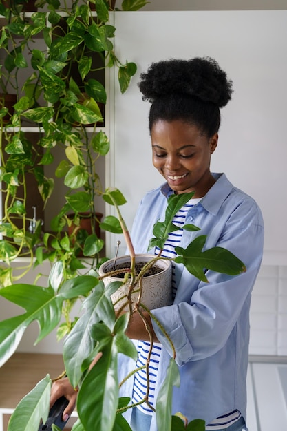 Joven afroamericana con una amplia sonrisa sostiene una planta de casa y examina la flor de Philodendron