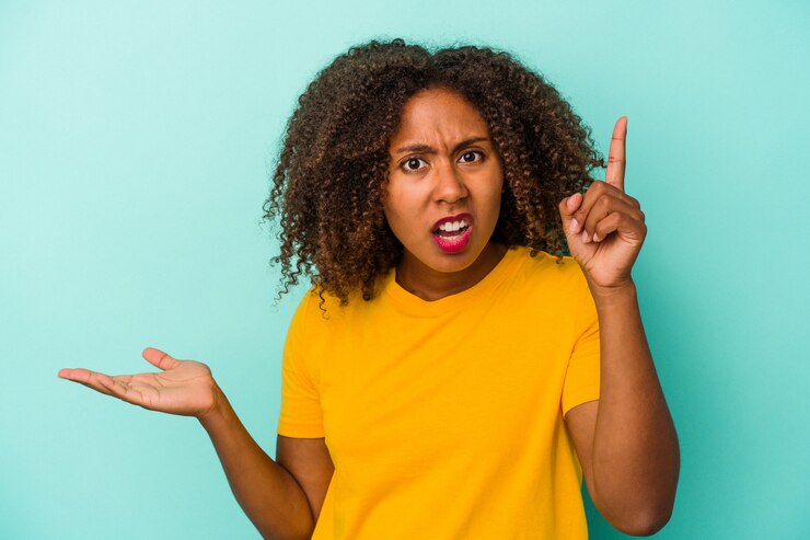 Foto joven afroamericana con cabello rizado aislado sobre fondo azul sosteniendo y mostrando un producto en la mano.