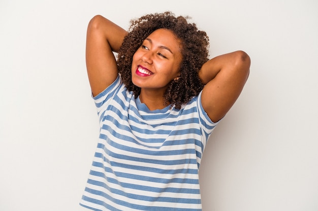 Joven afroamericana con cabello rizado aislado sobre fondo blanco sintiéndose confiado, con las manos detrás de la cabeza.