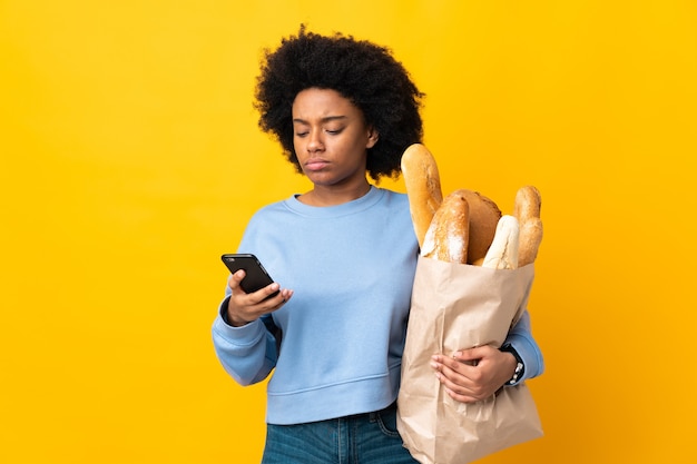 Joven afroamericana comprando algo de pan aislado en amarillo pensando y enviando un mensaje