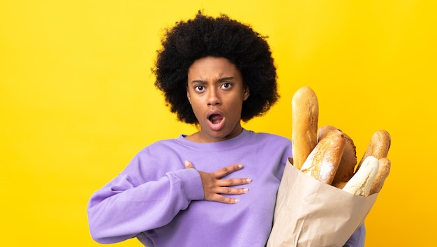 Joven afroamericana comprando algo de pan aislado en amarillo sorprendido y consternado mientras mira a la derecha