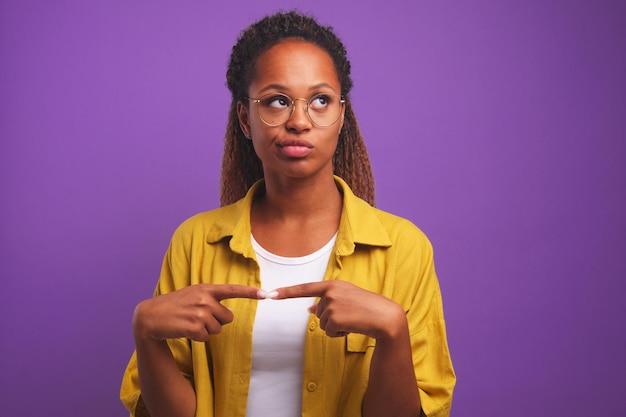 Joven afroamericana confundida con gafas redondas con una sonrisa mira hacia arriba