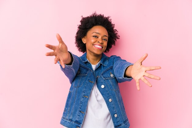 Joven afroamericana contra una pared rosa aislada se siente confiada dando un abrazo