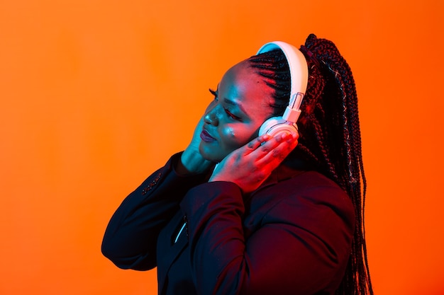 Joven afroamericana escuchando música en línea bailando y cantando con auriculares, neón