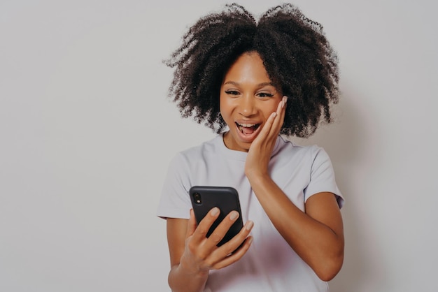 Una joven afroamericana feliz y llena de alegría recibe buenas noticias en un teléfono inteligente