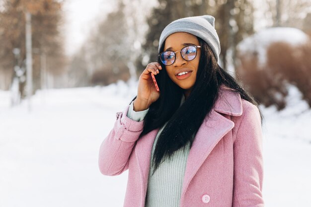 Una joven afroamericana con gafas y mitones calientes tomando por teléfono