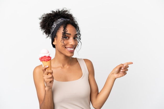 Joven afroamericana con un helado de cucurucho aislado sobre fondo blanco apuntando con el dedo hacia el lado