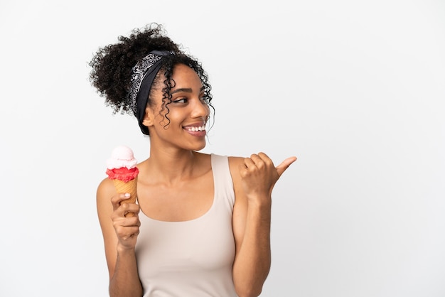 Joven afroamericana con un helado de cucurucho aislado sobre fondo blanco apuntando hacia el lado para presentar un producto