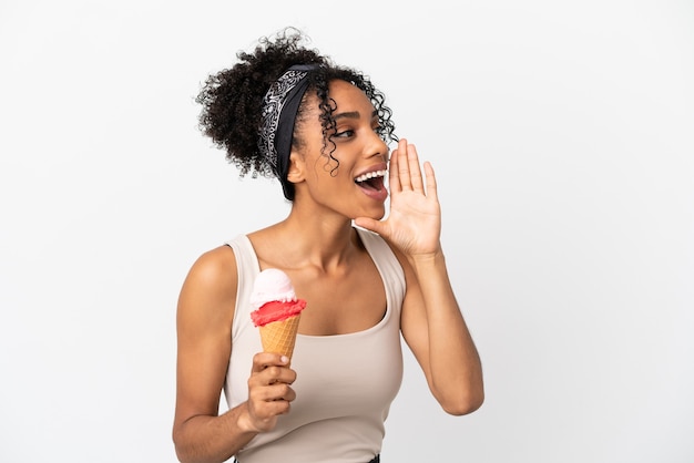 Joven afroamericana con un helado de cucurucho aislado sobre fondo blanco gritando con la boca abierta hacia el lado