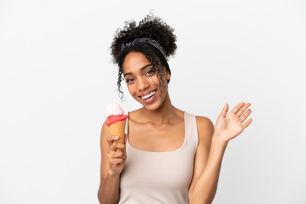 Joven afroamericana con un helado de cucurucho aislado sobre fondo blanco saludando con la mano con expresión feliz