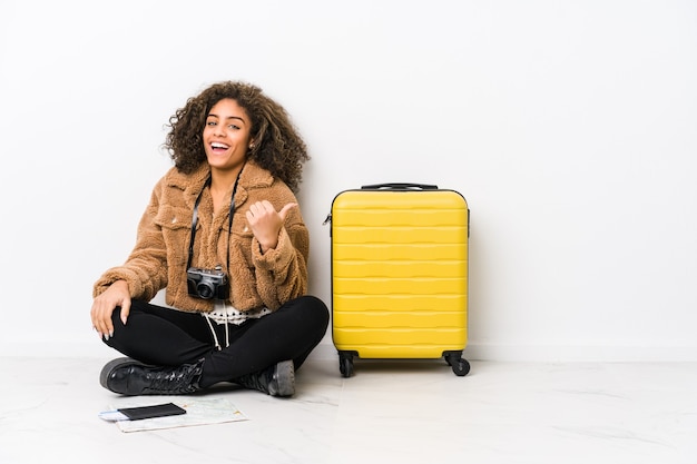 Joven afroamericana lista para un viaje apunta con el dedo pulgar, riendo y sin preocupaciones.