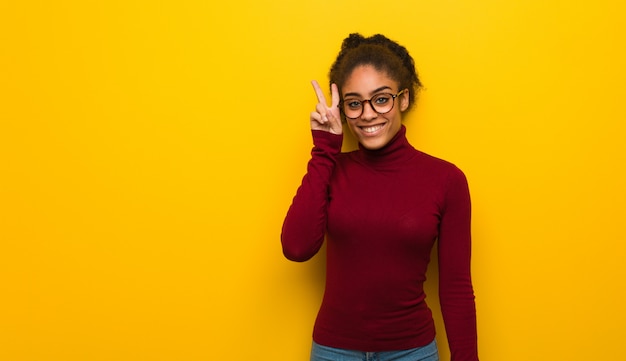 Joven afroamericana negra con ojos azules divertido y feliz haciendo un gesto de victoria