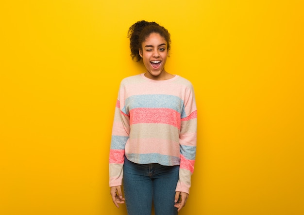 Joven afroamericana negra con ojos azules guiñando un ojo, gesto divertido, amable y despreocupado