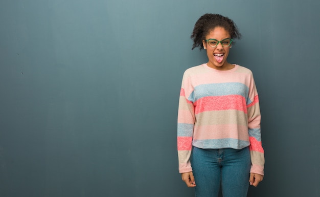 Joven afroamericana con ojos azules divertido y amigable mostrando lengua