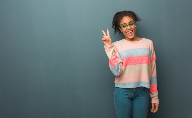 Joven afroamericana con ojos azules haciendo un gesto de victoria.