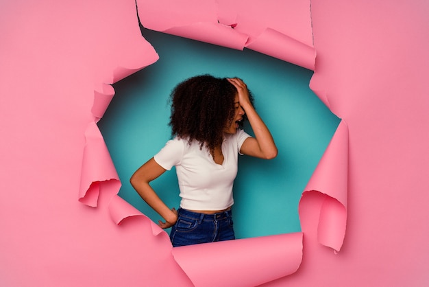 Foto joven afroamericana en papel rasgado aislado en azul olvidando algo, golpeándose la frente con la palma y cerrando los ojos.