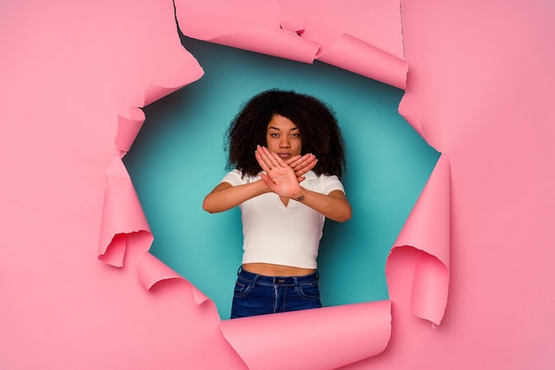 Joven afroamericana en papel rasgado aislado sobre fondo azul haciendo un gesto de negación