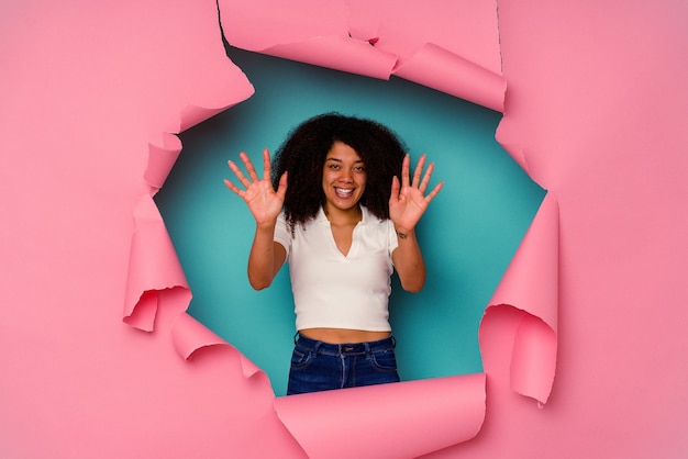 Joven afroamericana en papel rasgado aislado sobre fondo azul que muestra el número diez con las manos.