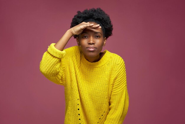 Joven afroamericana positiva mirando hacia la cámara con la mano sobre la frente buscando