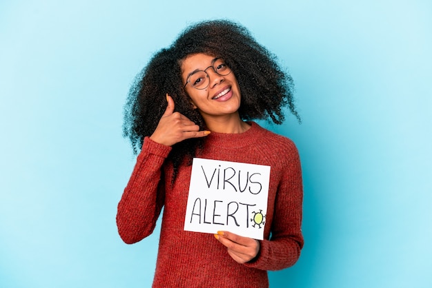 Joven afroamericana rizada sosteniendo un cartel de alerta de virus que muestra un gesto de llamada de teléfono móvil con los dedos.