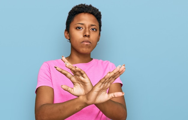 Joven afroamericana con ropa informal expresión de rechazo cruzando los brazos haciendo un signo negativo, cara enojada