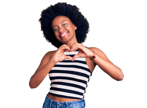 Joven afroamericana con ropa informal sonriendo enamorada mostrando el símbolo del corazón y la forma con las manos concepto romántico