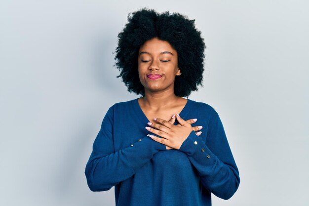 Joven afroamericana con ropa informal sonriendo con las manos en el pecho, los ojos cerrados con un gesto agradecido en la cara. concepto de salud