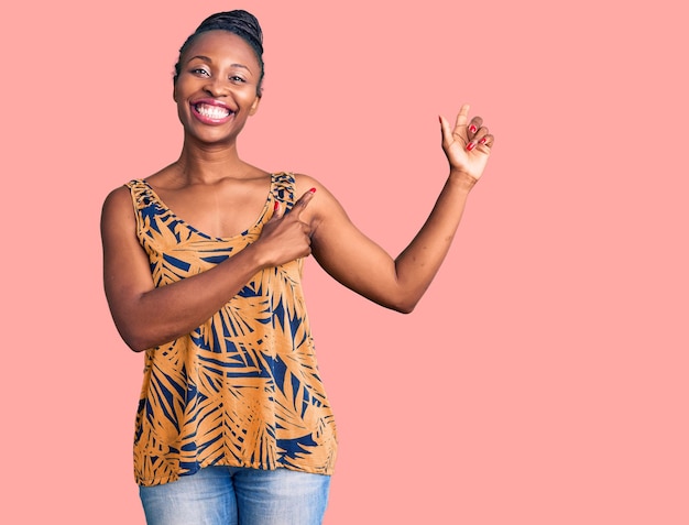 Joven afroamericana con ropa informal sonriendo y mirando a la cámara apuntando con dos manos y dedos a un lado