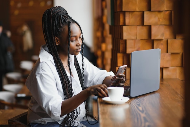 Joven afroamericana sentada en el restaurante y escribiendo en su computadora portátil Chica guapa trabajando en la computadora en el café