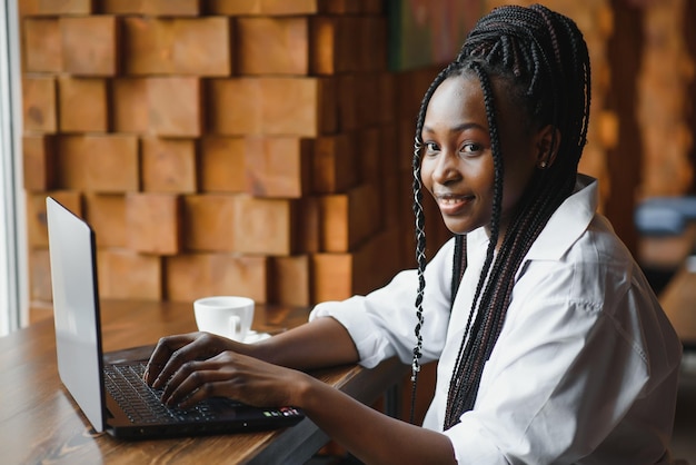 Joven afroamericana sentada en el restaurante y escribiendo en su computadora portátil Chica guapa trabajando en la computadora en el café