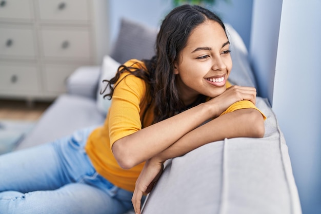 Joven afroamericana sonriendo confiada sentada en el sofá en casa