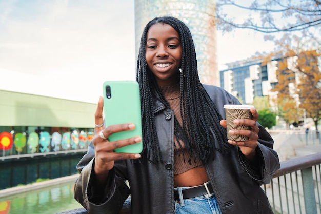 Joven afroamericana sonriendo y escribiendo con la aplicación de teléfono celular Adolescente feliz enviando mensajes usando un teléfono inteligente después de ir de compras al aire libre Concepto de comunicación Cámara lenta