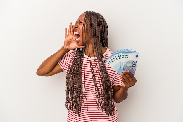 Joven afroamericana sosteniendo billetes aislados sobre fondo blanco gritando y sosteniendo la palma cerca de la boca abierta.