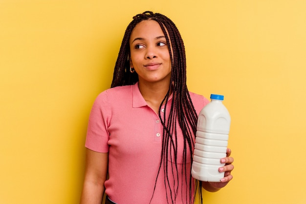 Joven afroamericana sosteniendo una botella de leche aislada en la pared amarilla soñando con lograr metas y propósitos