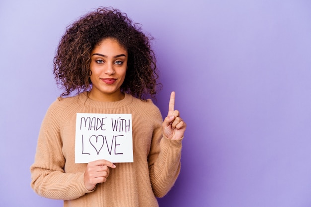 Joven afroamericana sosteniendo un cartel hecho con amor aislado en la pared púrpura que muestra el número uno con el dedo.