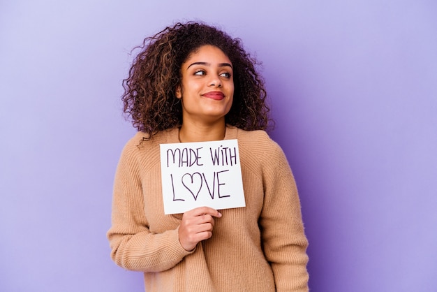 Joven afroamericana sosteniendo un cartel hecho con amor aislado sobre fondo púrpura soñando con lograr metas y propósitos