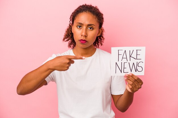 Joven afroamericana sosteniendo cartel de noticias falsas aislado sobre fondo rosa