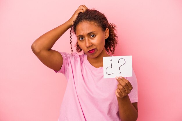 Joven afroamericana sosteniendo un cartel de preguntas aislado de fondo rosa