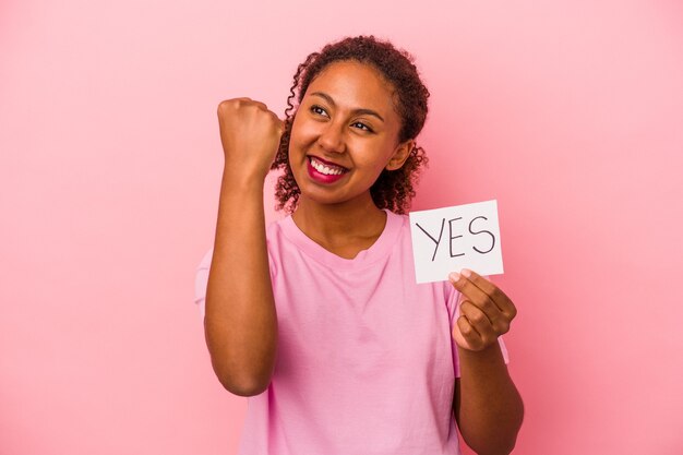 Joven afroamericana sosteniendo un cartel de sí aislado sobre fondo de color rosa