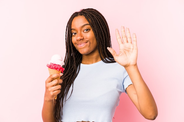 Joven afroamericana sosteniendo un helado aislado sonriendo alegre mostrando el número cinco con los dedos.