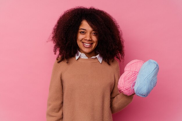 Joven afroamericana sosteniendo un hilo de coser aislado en rosa feliz, sonriente y alegre.