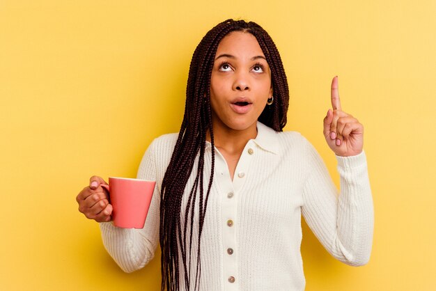 Joven afroamericana sosteniendo una taza aislada apuntando hacia arriba con la boca abierta