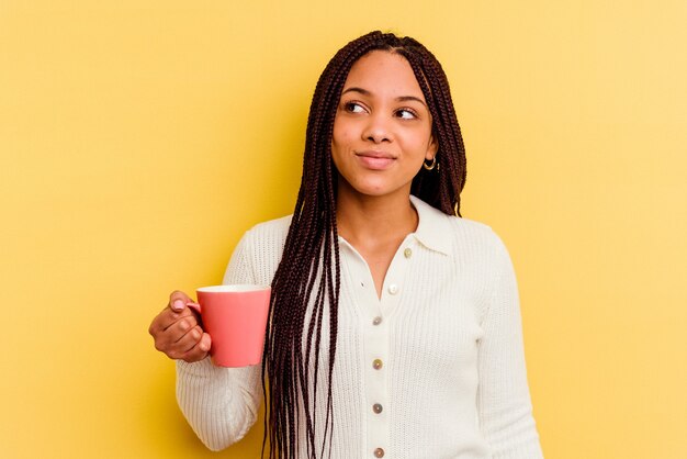 Joven afroamericana sosteniendo una taza aislada soñando con lograr metas y propósitos