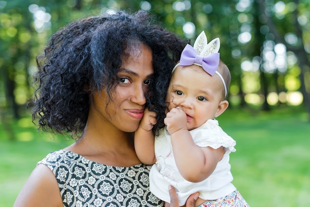 Joven afroamericana y su hija sonriendo caminando en el parque de verano.