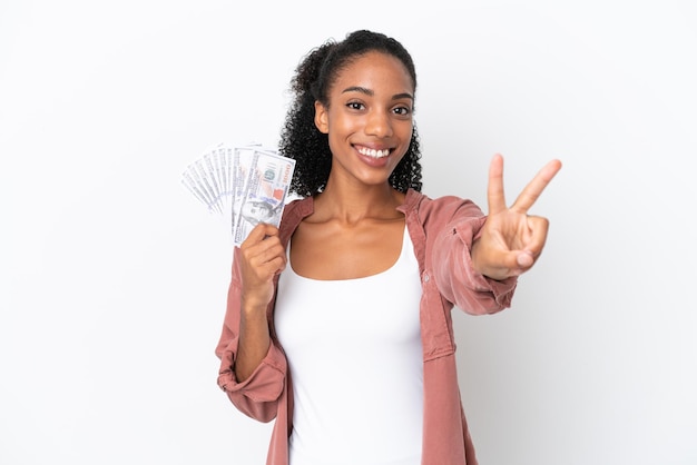 Joven afroamericana tomando un montón de dinero aislado sobre fondo blanco sonriendo y mostrando el signo de la victoria