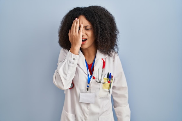 Joven afroamericana con uniforme médico y estetoscopio bostezando cansada cubriendo la mitad de la cara, los ojos y la boca con la mano. la cara duele de dolor.